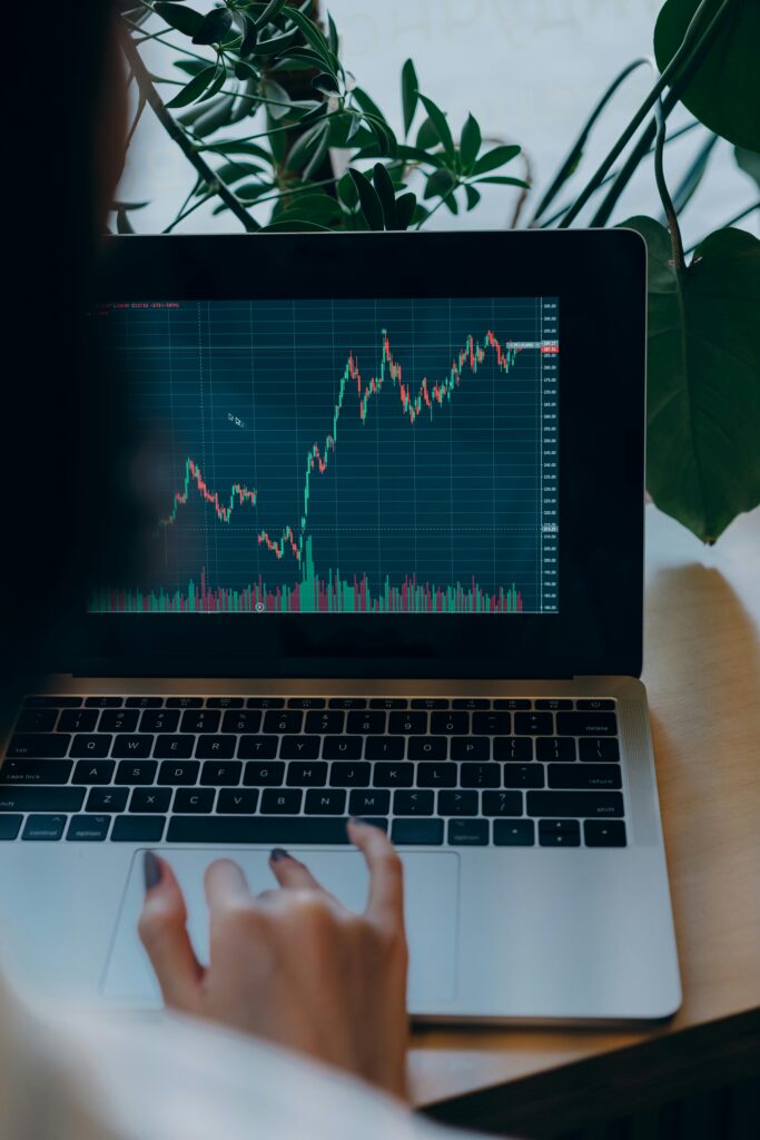 Person using laptop displaying stock market graph amidst indoor plants.