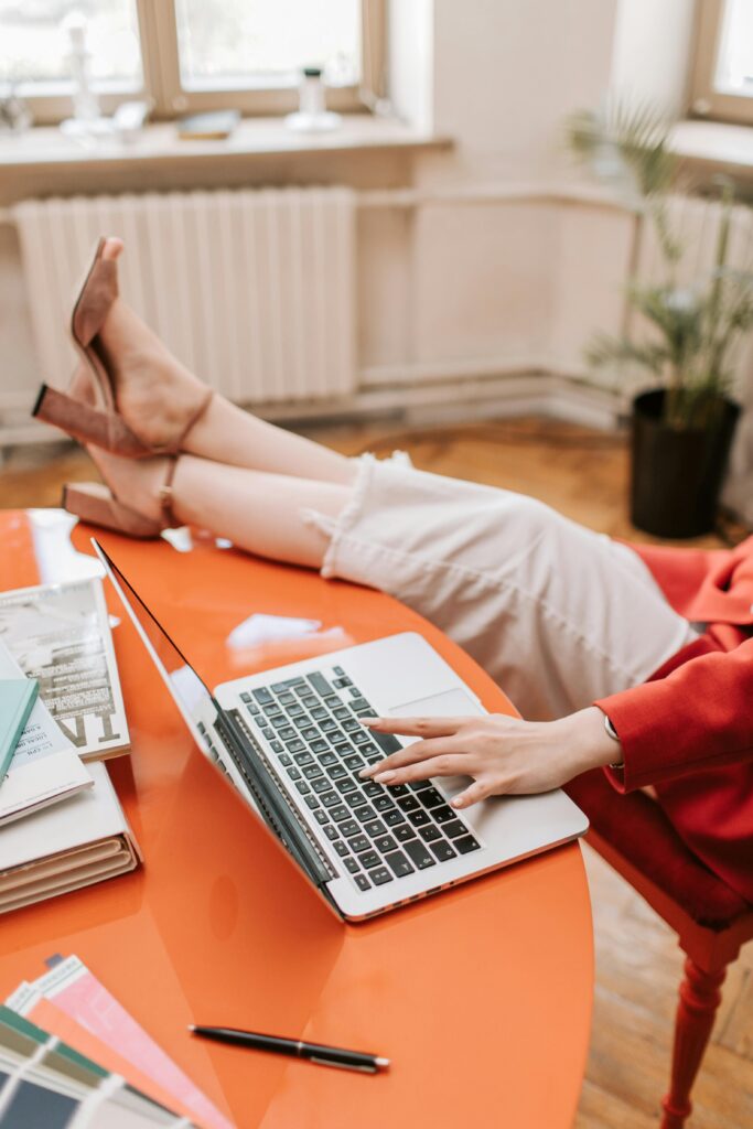 Woman wearing heels and working on a laptop at home, relaxed and casual setting.